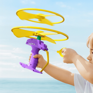 Child playing with a purple and yellow outdoor flying toy on a beach against a blue sky