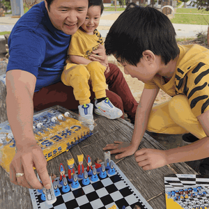 Family playing with Educational Wooden Cartoon Chess Set outdoors on wooden table